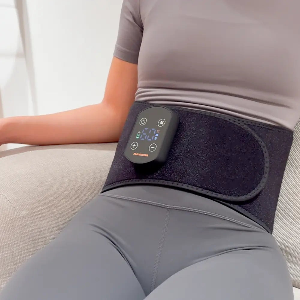 Woman wearing the PainRelieva™ heated back massager belt around her waist while sitting comfortably on a sofa